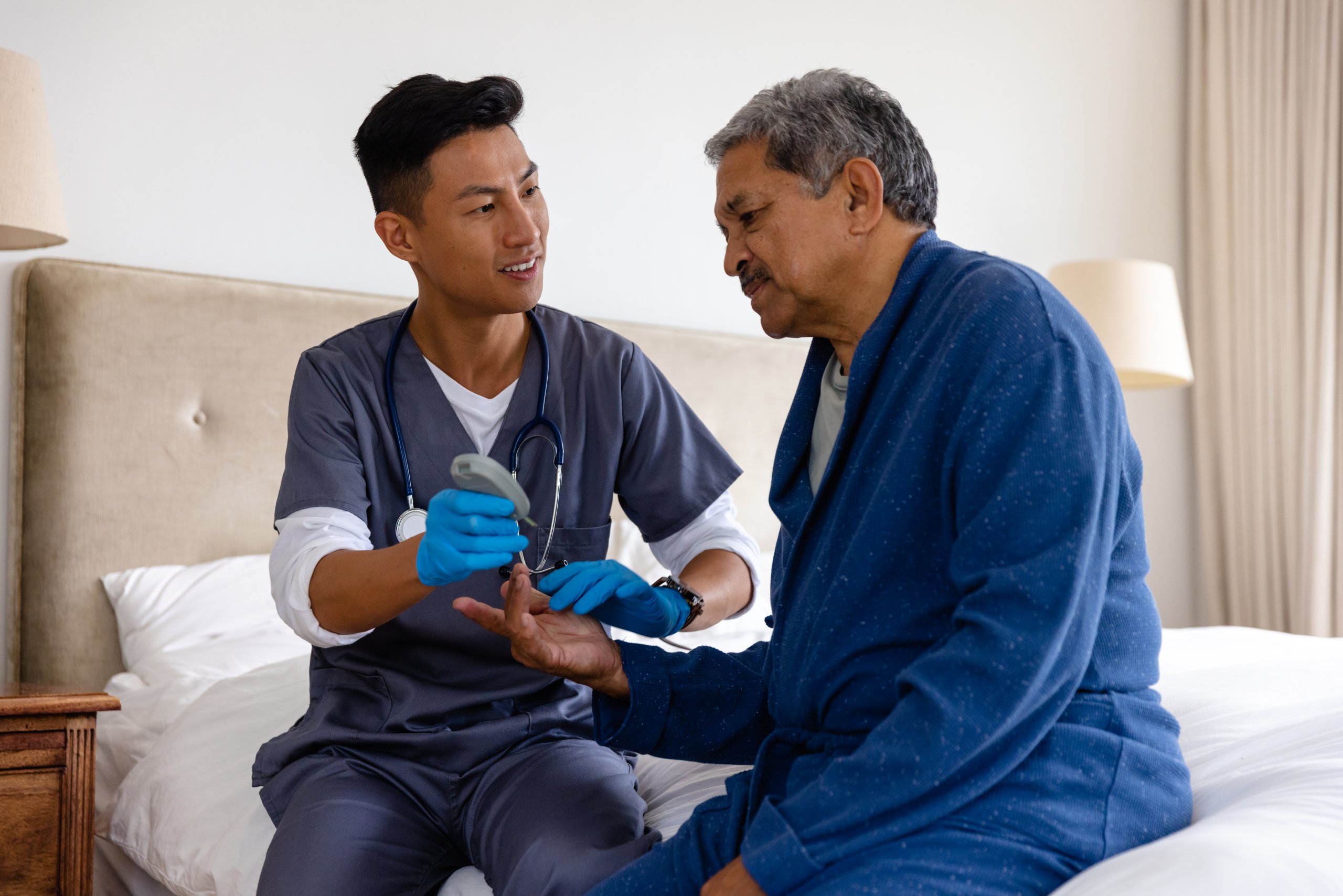 Diverse male doctor testing blood of senior male patient at home. Medical services, check up, home visit, healthcare, wellbeing and senior lifestyle, unaltered. End of life caregiver helping patient through the misconceptions about hospice care